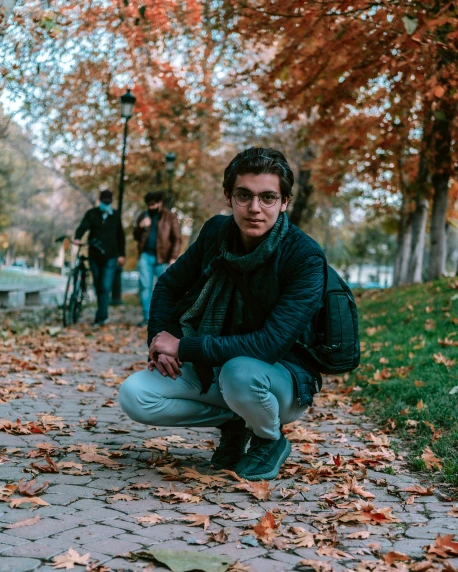 a man squatting on the ground in a park, an album cover, by Ismail Acar, pexels contest winner, antipodeans, 🍁 cute, lgbt, late autumn, looking the camera