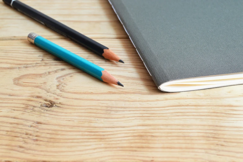 a notebook and two pencils on a wooden table, by Carey Morris, pexels contest winner, academic art, 9 9 designs, grey, teal paper, close up portrait shot