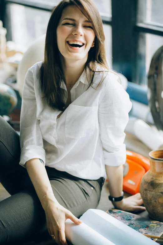 a smiling woman sitting on the floor next to a vase, inspired by Peter de Sève, pexels contest winner, renaissance, wearing a white button up shirt, in a workshop, profile image, manically laughing