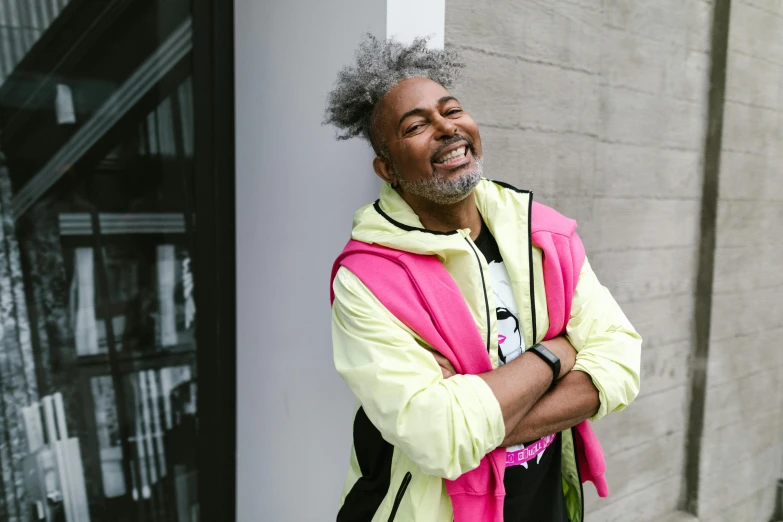 a man leaning against a wall with his arms crossed, by Winona Nelson, happening, wearing a pink hoodie, laughing man, aida muluneh, bright neon highlights
