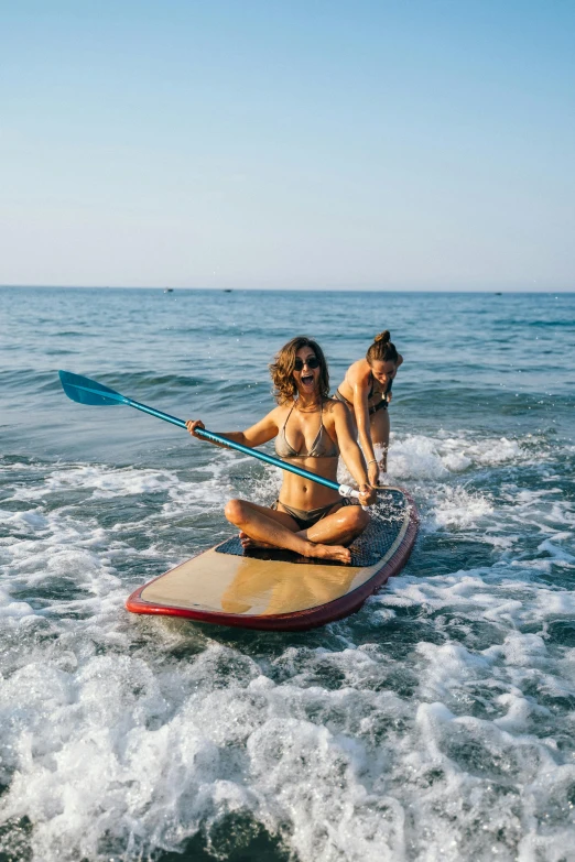 a couple of women riding on top of a surfboard, paddle of water, square, marbella, onsens