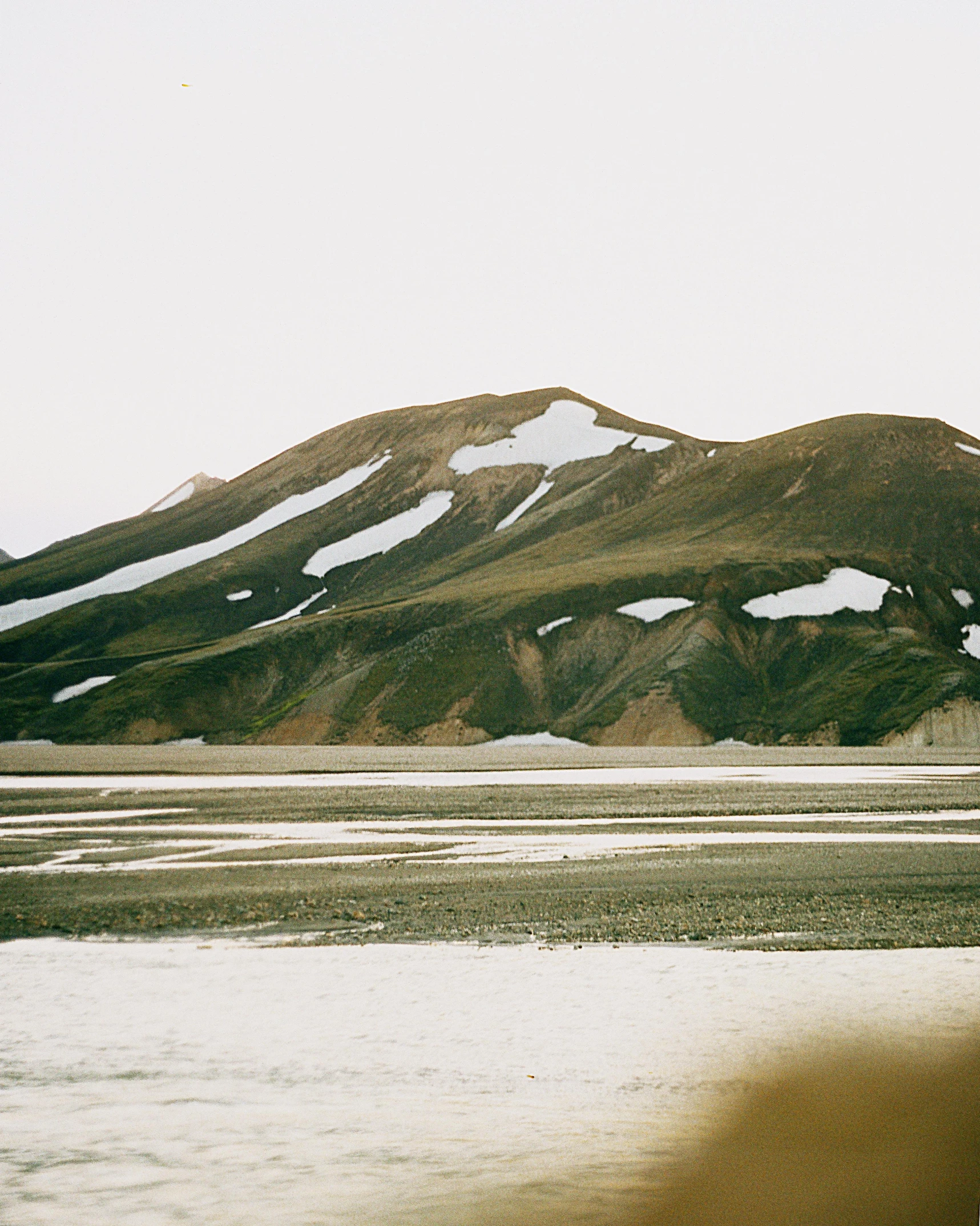 a mountain covered in snow next to a body of water, by Hallsteinn Sigurðsson, trending on unsplash, land art, brown skin like soil, muted pastel colors, sand dunes, soft vinyl