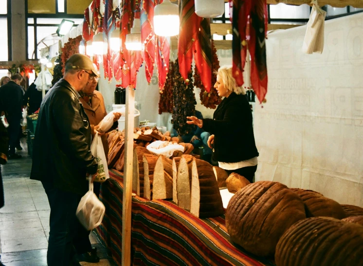 a group of people standing around a food stand, crafts and souvenirs, winter season, maroon, indoor