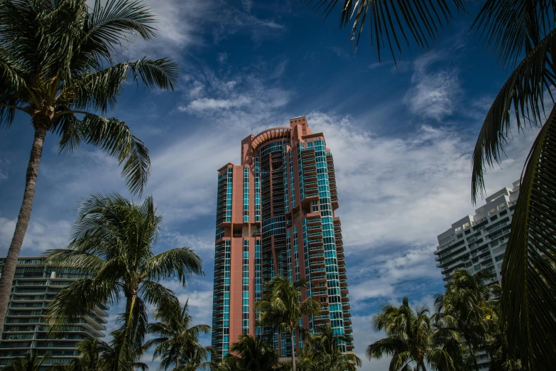 a tall building surrounded by palm trees on a sunny day, by Robbie Trevino, pexels contest winner, pink and teal and orange, slide show, miami, thumbnail