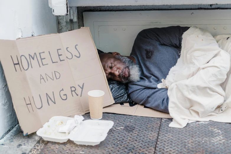 a homeless man is sleeping on the sidewalk, by Matija Jama, pexels contest winner, renaissance, mukbang, samuel jackson, cardboard, on a gray background