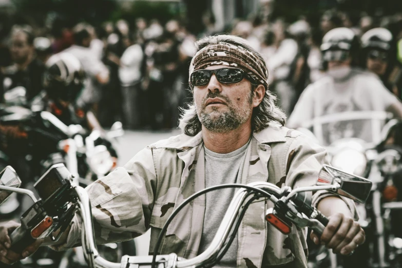 a man riding on the back of a motorcycle down a street, a colorized photo, pexels contest winner, photorealism, wearing a bandana and chain, jason momoa, crowd, portrait of a us navy seal