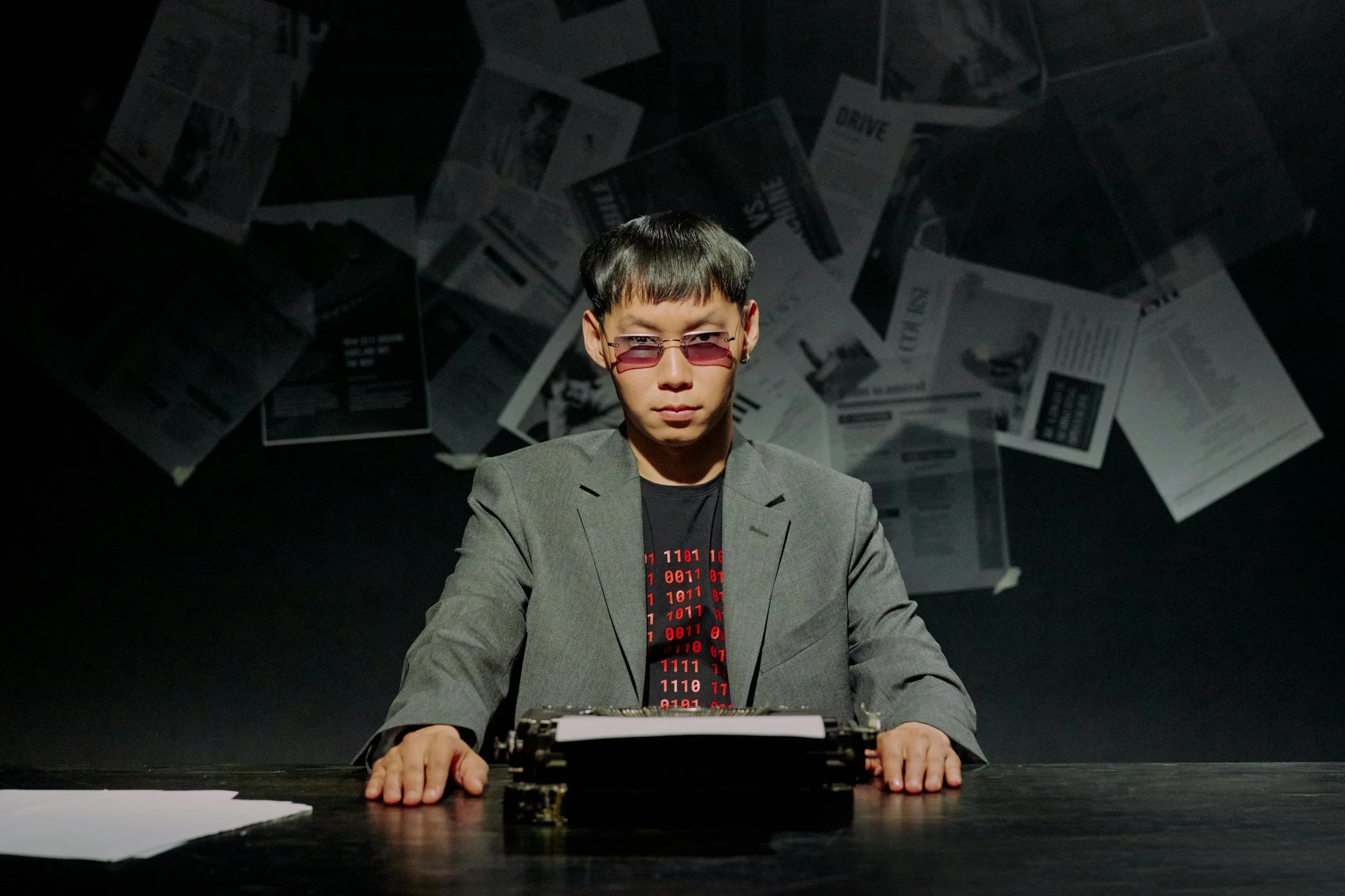 a man sitting at a table with a typewriter in front of him, neo-dada, andy milonakis, production photo, wearing a suit and glasses, photographed for reuters