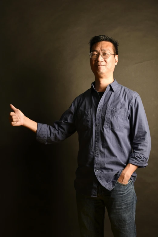 a man standing in front of a black wall, inspired by Fei Danxu, happening, wearing a shirt and a jean, nerd, pointing at the camera, slight overcast lighting