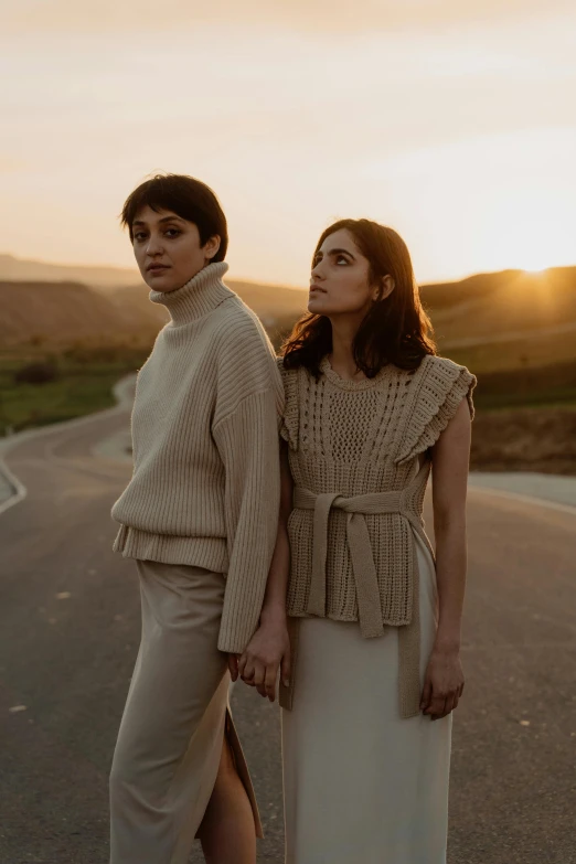 two people standing next to each other on a road, an album cover, by Winona Nelson, trending on pexels, renaissance, young women, hila klein, sweater, soft evening lighting