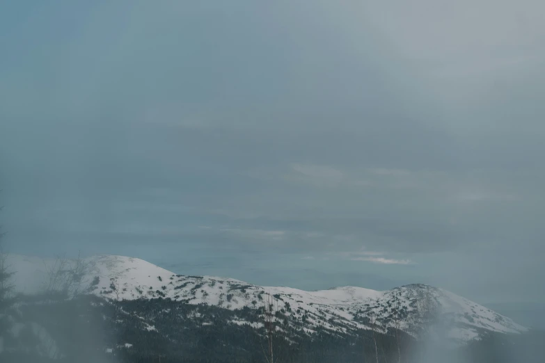 a group of people riding skis on top of a snow covered slope, by Roar Kjernstad, trending on unsplash, hurufiyya, gray sky with wispy clouds, landscape from a car window, 4 k cinematic panoramic view, distant mountains lights photo