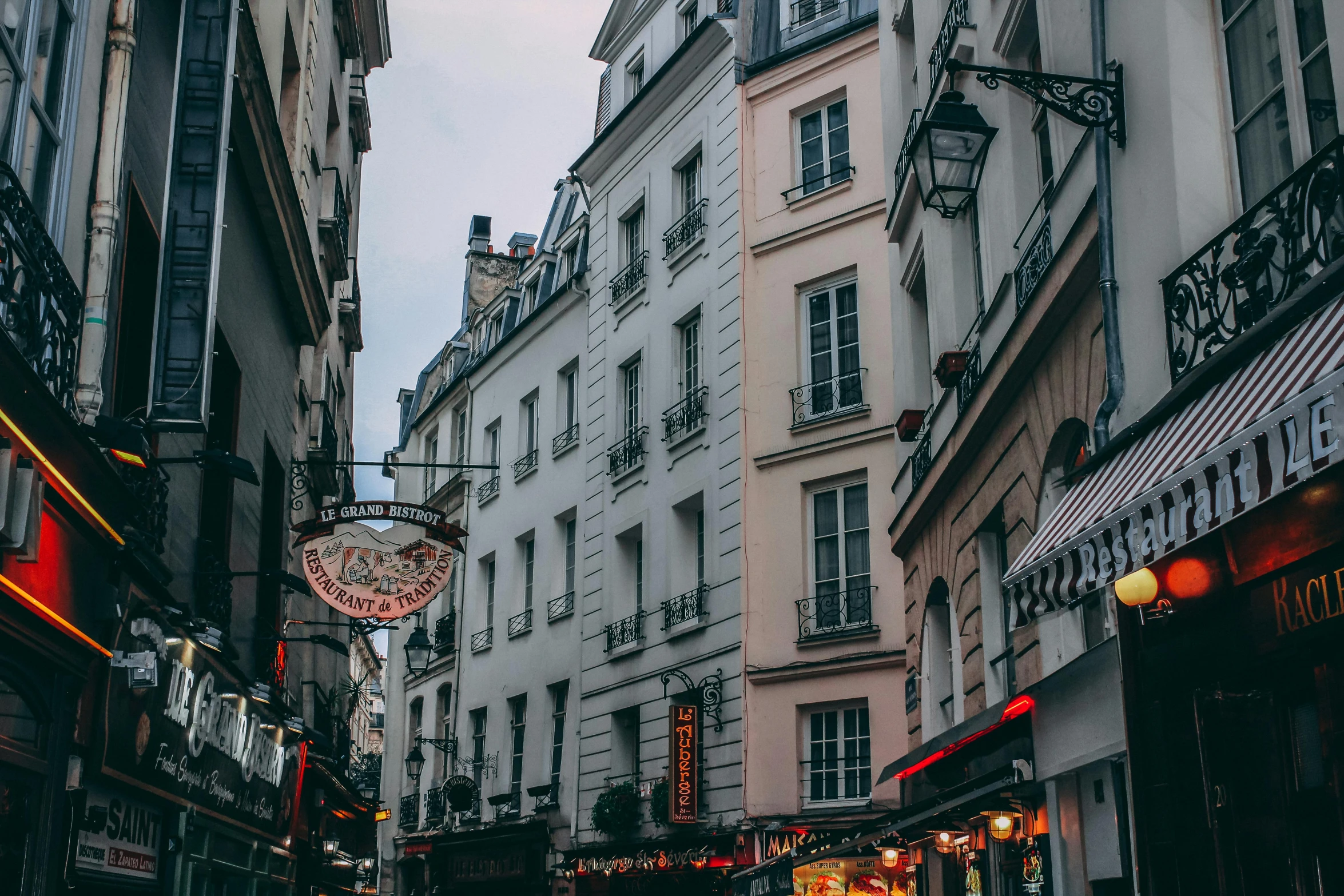 a group of people walking down a street next to tall buildings, pexels contest winner, paris school, old shops, cozy, colorful signs, french noveau