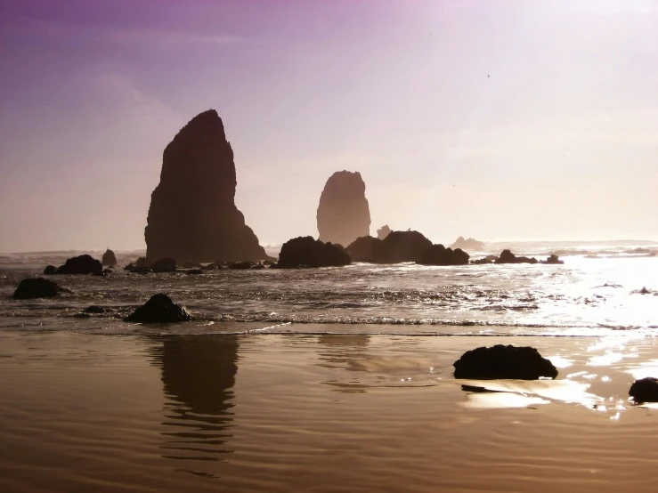 a couple of rocks sitting on top of a sandy beach, chrome cathedrals, an ocean