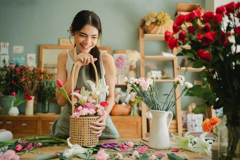 a woman sitting at a table with a basket of flowers, pexels contest winner, arts and crafts movement, she is smiling and excited, flower shop scene, asian women, roses in hands