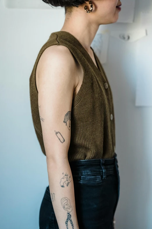 a woman with a tattoo on her arm, by Niko Henrichon, trending on pexels, tan vest, non binary model, wearing a cardigan, wearing : tanktop