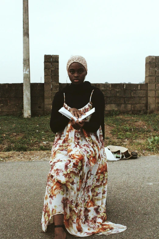 a woman sitting on the ground reading a book, an album cover, by Chinwe Chukwuogo-Roy, pexels contest winner, happening, standing in a township street, islamic, wide film still, full body with costume