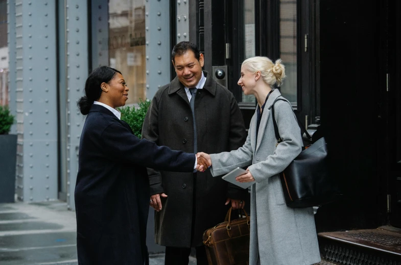 a group of people shaking hands in front of a building, trench coat and suit, ignant, amanda lilleston, varying ethnicities