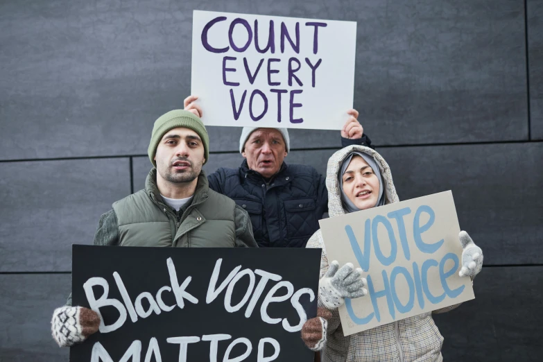 a group of people holding signs in front of a building, a photo, by Dan Frazier, shutterstock, mostly black, the three moiras, victor antonov, against all odds