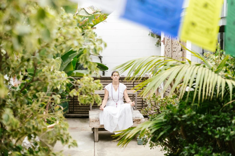 a woman sitting on a bench in a garden, kundalini energy, in a white boho style studio, pyramid surrounded with greenery, stressing out