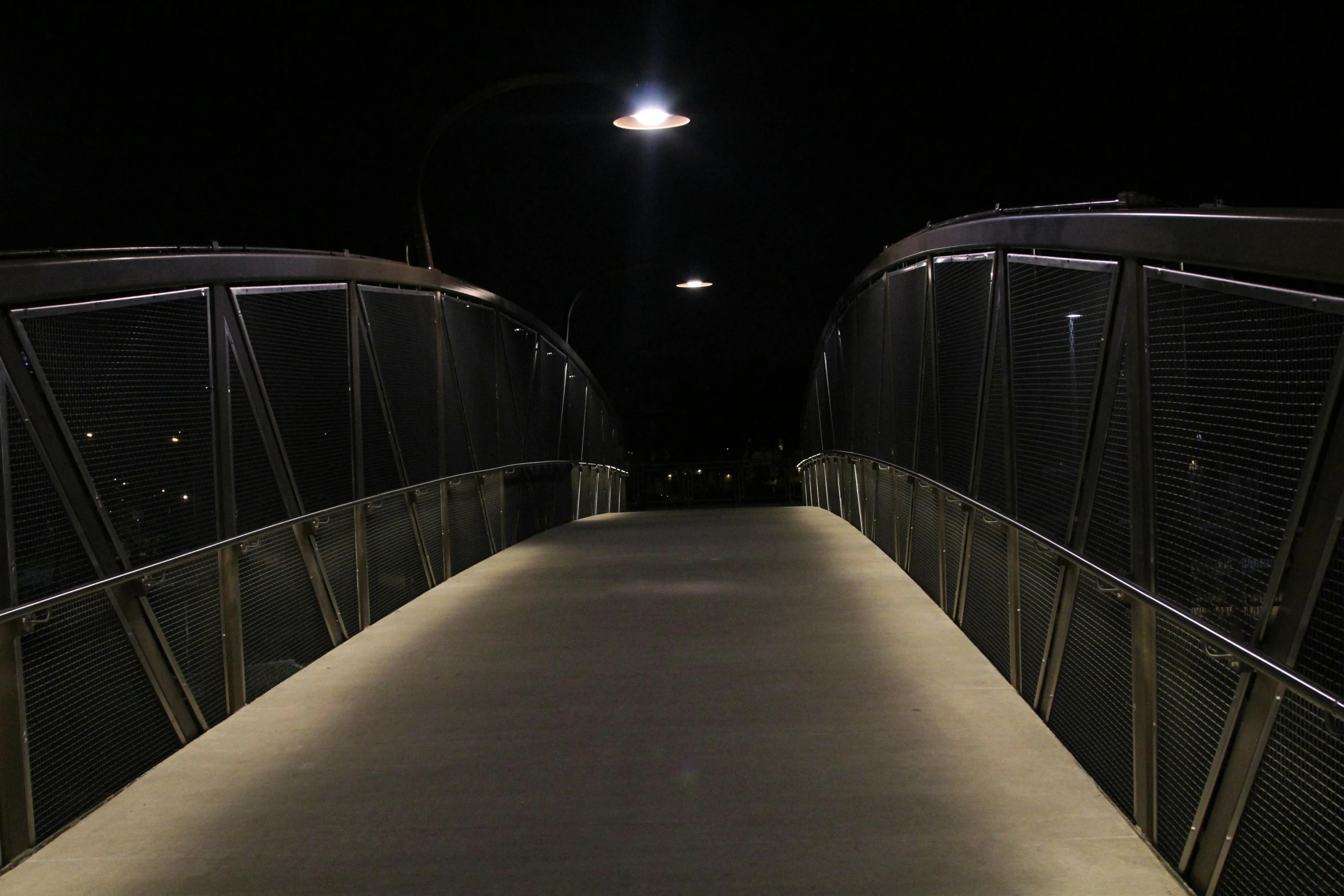 a person walking across a bridge at night, award winning lighting, calm lighting, overhead lighting, it's dark