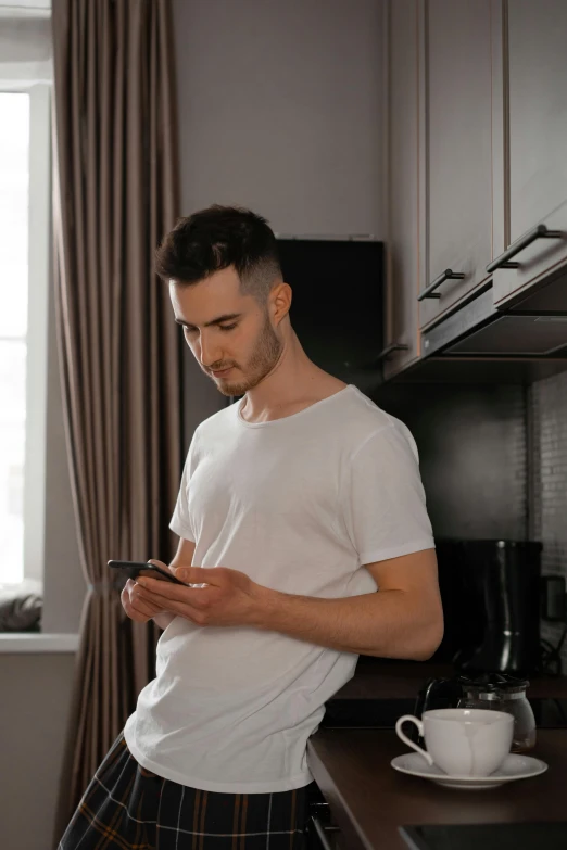 a man standing in a kitchen looking at his cell phone, trending on pexels, renaissance, non binary model, tight shirt, avatar image, maxim sukharev