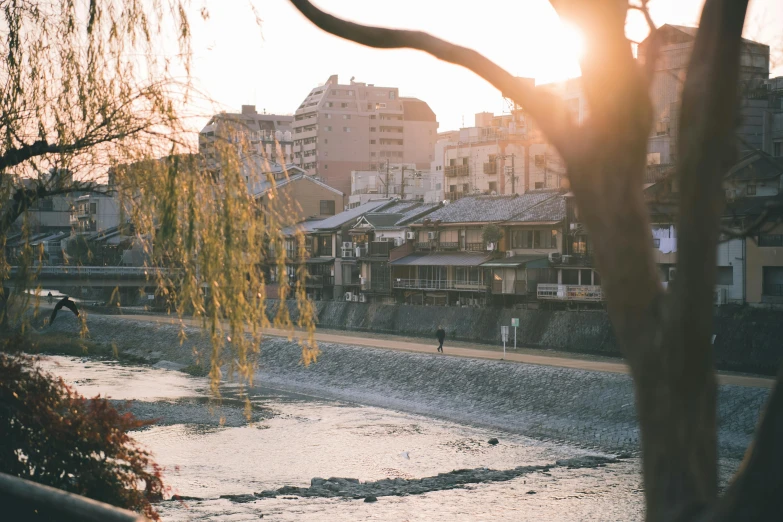 a view of a river with buildings in the background, inspired by Tōshi Yoshida, pexels contest winner, winter sun, sasoura, people walking in the distance, beautiful small town