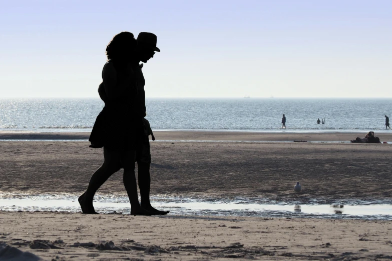 a woman standing on top of a sandy beach, by Jan Gregoor, unsplash, romanticism, man and woman walking together, detailed silhouette, straw hat and overcoat, dunkirk