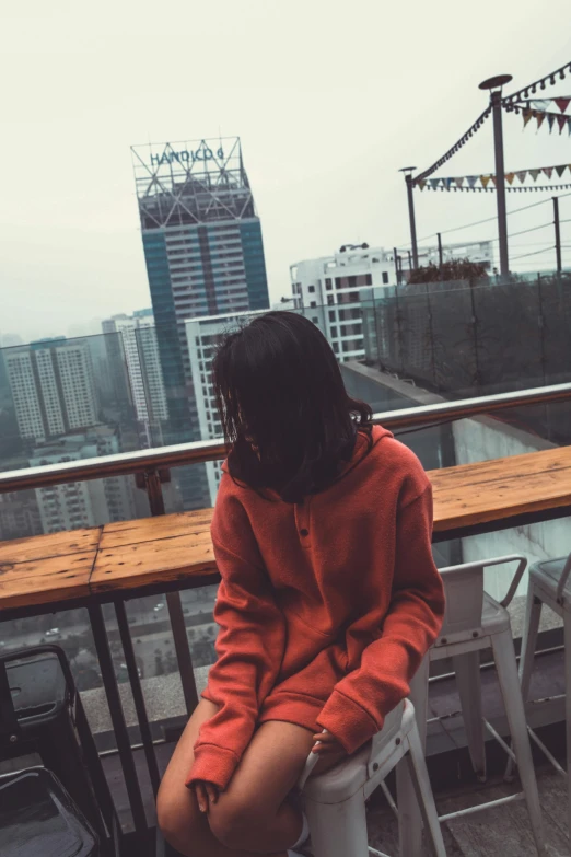 a woman sitting on top of a white stool, inspired by Elsa Bleda, unsplash contest winner, long orange sweatshirt, set in tokyo rooftop, grainy. poorly rated, male ulzzang