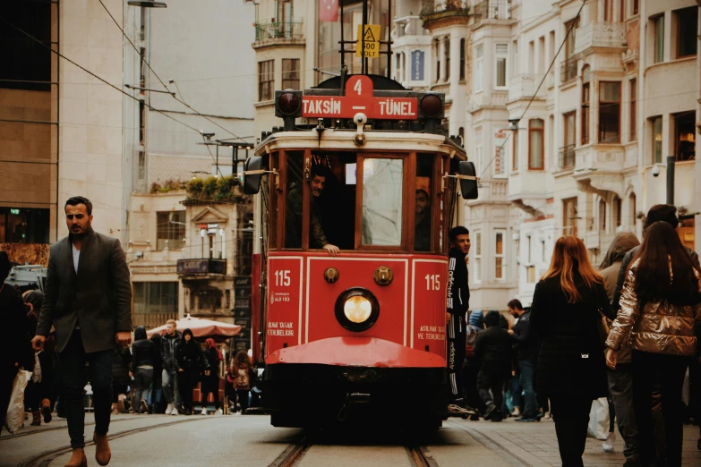 a red trolley traveling down a street next to tall buildings, by Matija Jama, pexels contest winner, art nouveau, ottoman empire, brown, subtitles, 🦩🪐🐞👩🏻🦳