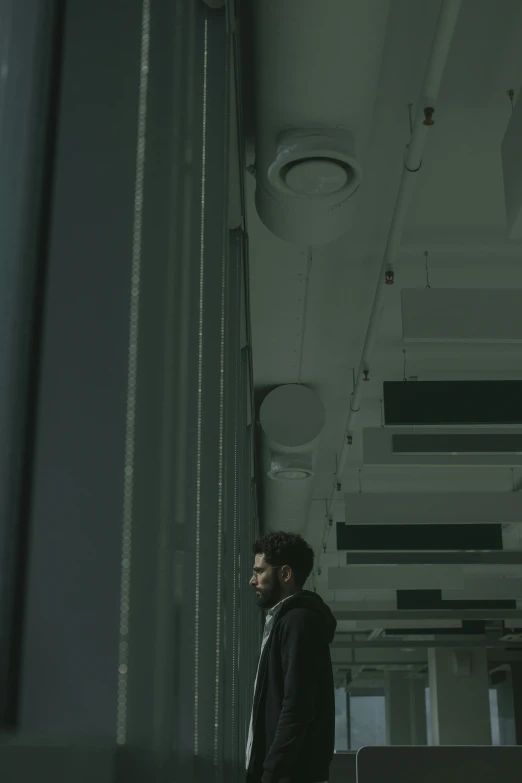 a man standing next to a window in a building, inspired by Elsa Bleda, standing in a server room, **cinematic, underexposed grey, ( ( theatrical ) )
