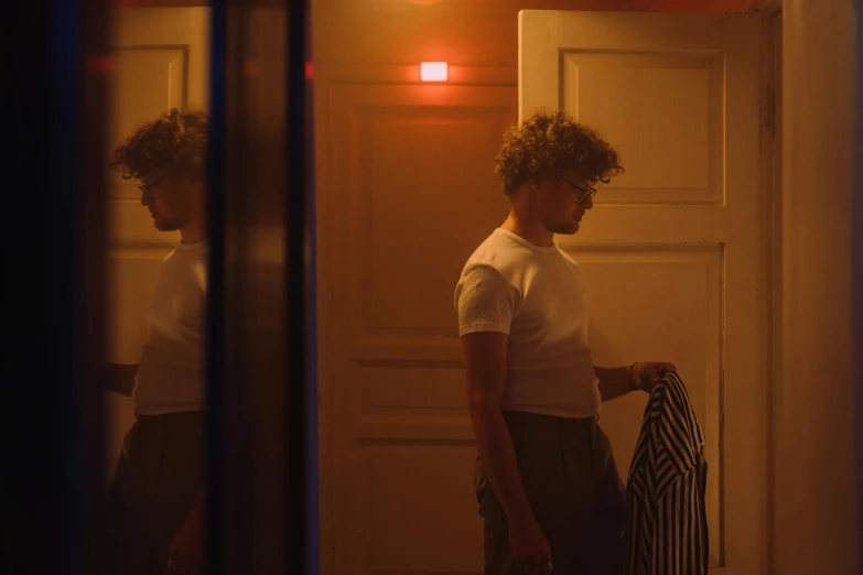 a woman standing in a hallway next to a door, inspired by Nan Goldin, pexels, serial art, he has short curly brown hair, soft calm warm neon atmosphere, teenage boy, looking in the mirror