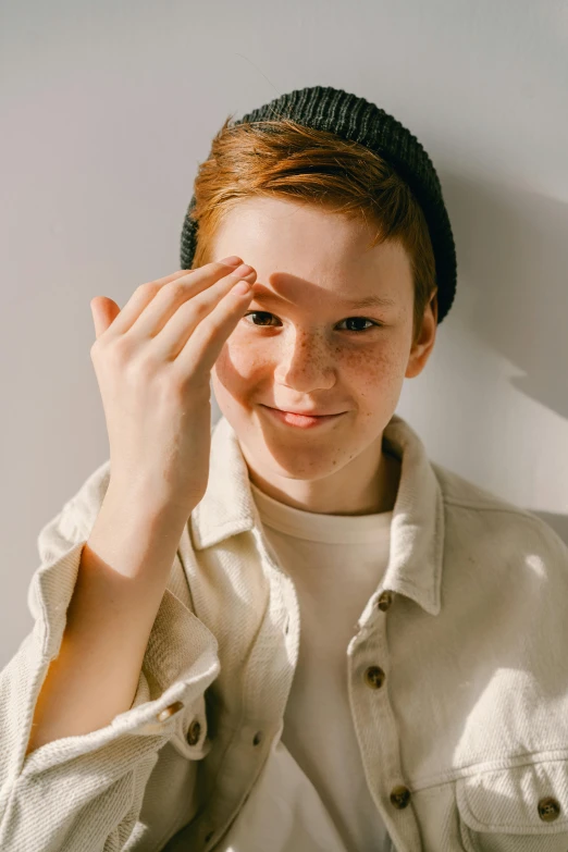 a close up of a person wearing a hat, red haired teen boy, groomed eyebrows, greeting hand on head, non binary model