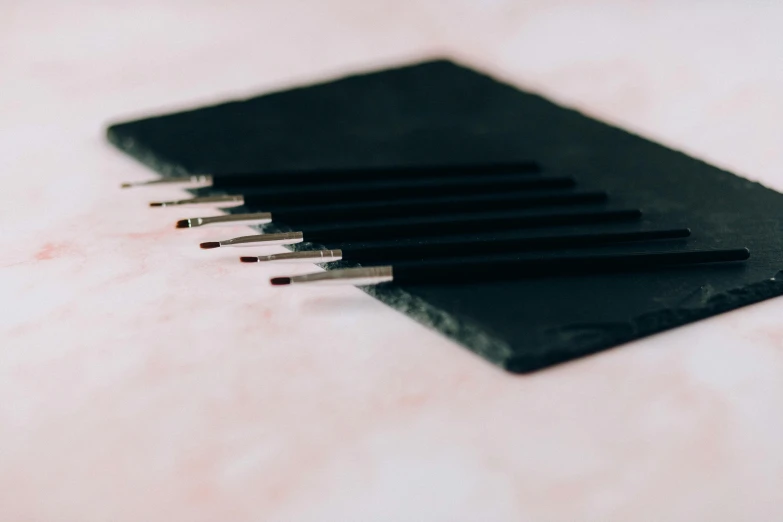 a group of pencils sitting on top of a piece of paper, a charcoal drawing, inspired by Lucio Fontana, unsplash, kinetic pointillism, minimal pink palette, made of smooth black goo, close-up product photo, surgical implements