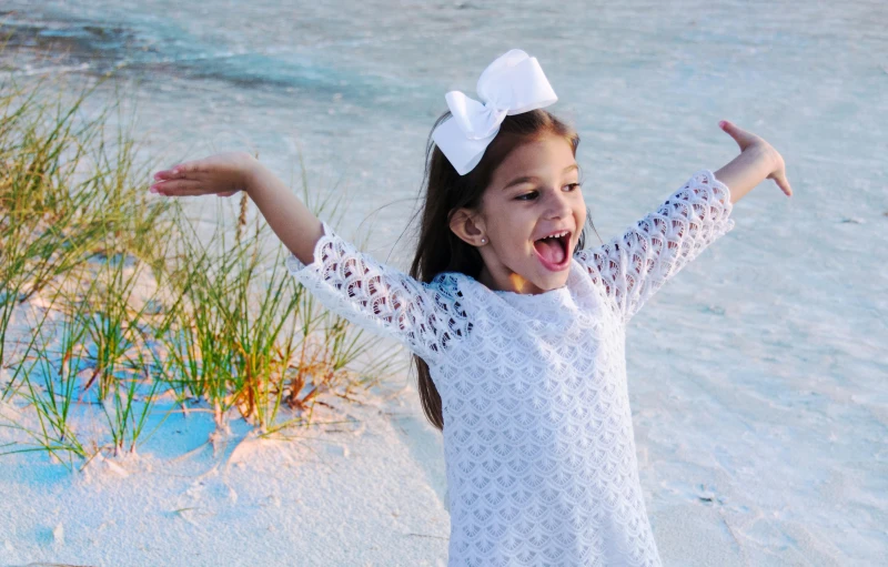 a little girl standing on top of a sandy beach, girl in white dress dancing, earing a shirt laughing, 2019 trending photo, full frame image