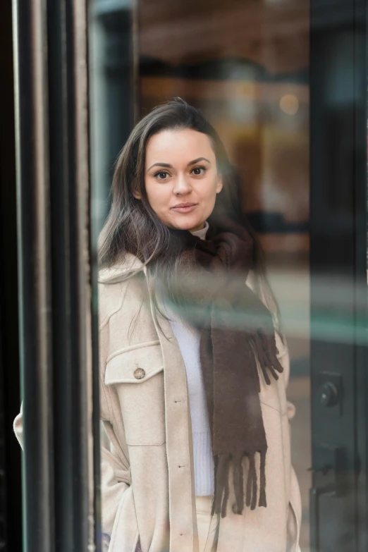 a woman standing in front of a glass door, a portrait, inspired by Louisa Matthíasdóttir, pexels contest winner, hurufiyya, exiting store, girl with dark brown hair, white scarf, light brown coat