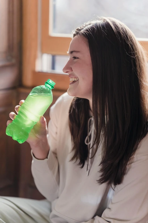 a woman sitting on a bed holding a bottle of water, pexels contest winner, vibrant green, 🍸🍋, college, translucent