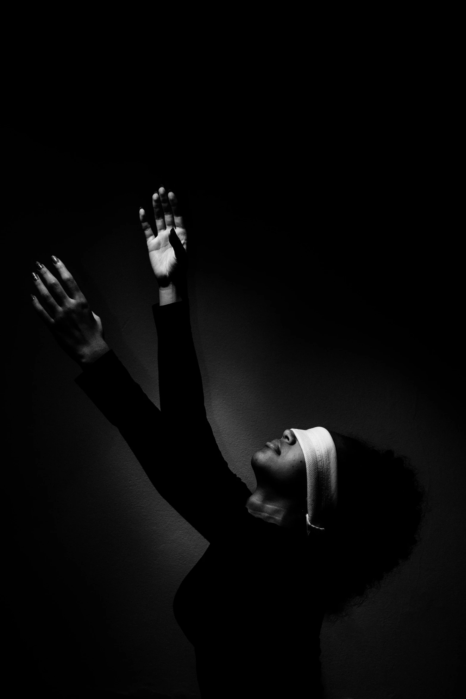 a black and white photo of a woman with her hands in the air, an album cover, inspired by Carrie Mae Weems, unsplash, blindfolded, praying meditating, light bends to him, black black black woman