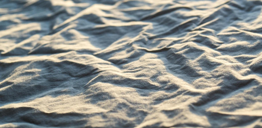 a close up of a blanket on a bed, an ambient occlusion render, unsplash, beach sand background, rendered in unreal engine 4k hq, low sun, pbr textures