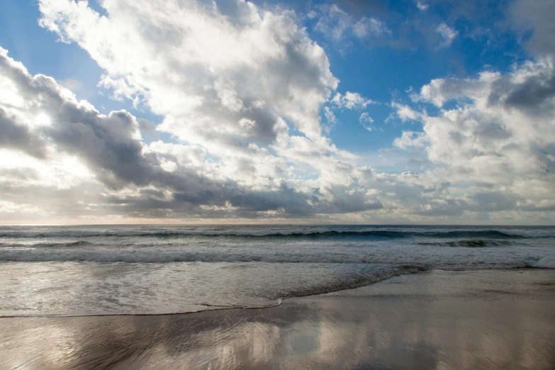 a man riding a surfboard on top of a sandy beach, voluminous clouds, blue reflections, “ iron bark, panoramic photography