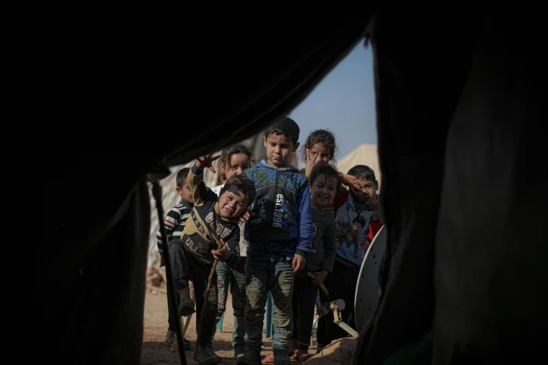 a group of people standing in front of a tent, by Micha Klein, trending on unsplash, hurufiyya, ap press photo, children, dressed in a worn, bl