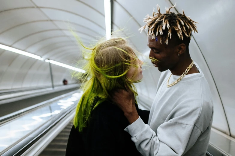 a man standing next to a woman on an escalator, a photo, trending on pexels, afrofuturism, bright green hair, holding each other, messy blond hair, white highlights in hair