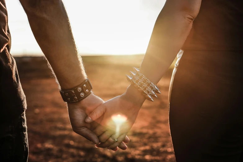 a man and a woman holding hands in a field, pexels, leather cuffs around wrists, outback, sun overhead, instagram post