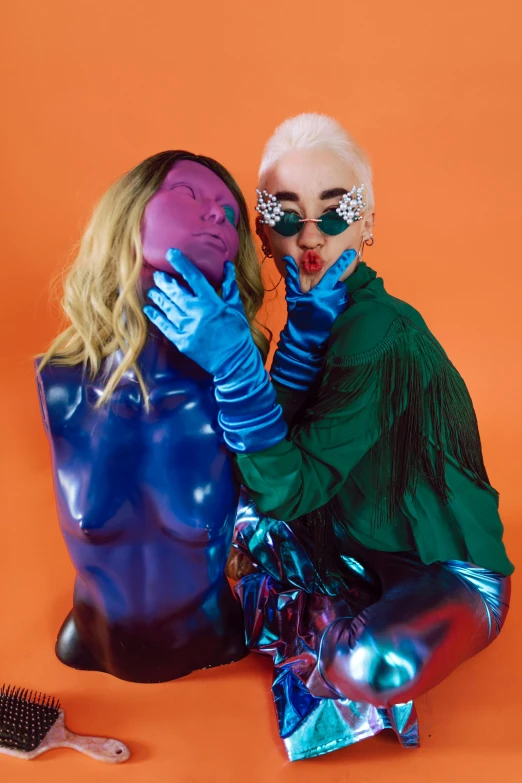 a couple of women sitting next to each other, an album cover, inspired by David LaChapelle, trending on pexels, antipodeans, futuristic glossy latex suit, sleek hands, dayglo blue, a blond