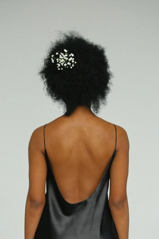 a woman in a black dress with a flower in her hair, bare back, afro tech, white pearlescent, ari aster