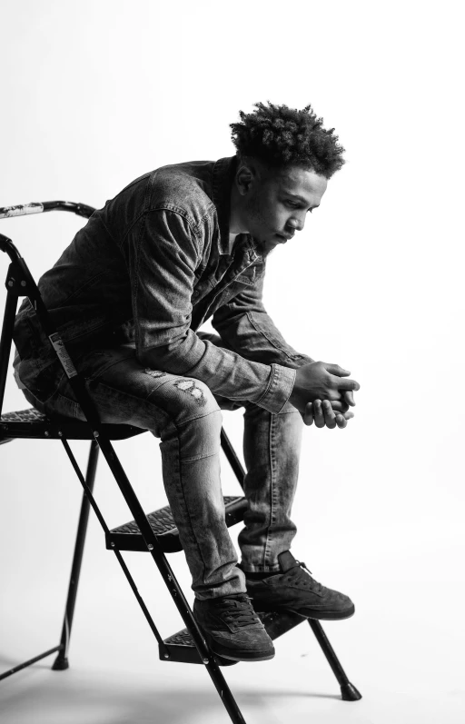 a black and white photo of a man sitting on a chair, xxxtentacion, jeffery smith, profile pose, dressed in a worn