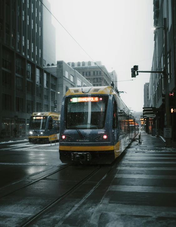 a train traveling down a city street next to tall buildings, during a storm, minneapolis, non-binary, trams