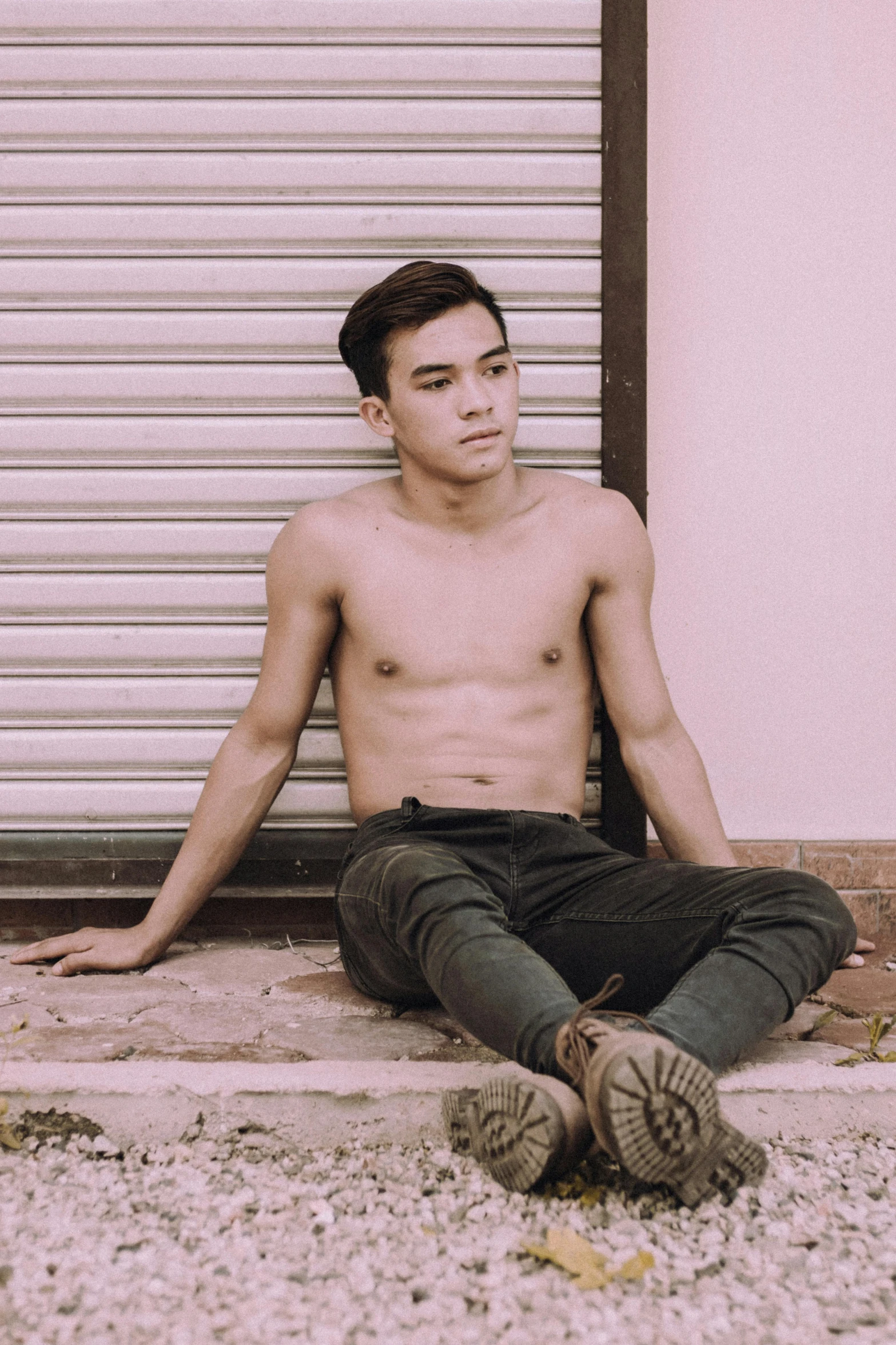 a man sitting on the ground in front of a garage door, inspired by David Diao, unsplash, non binary model, physical : tinyest midriff ever, malaysian, ruan cute vtuber