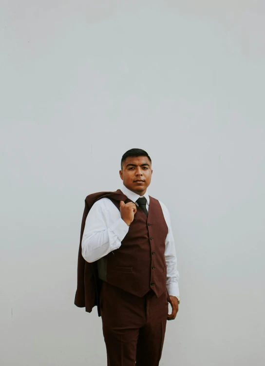 a man in a suit and tie standing in front of a white wall, an album cover, by Carey Morris, unsplash, renaissance, brown suit vest, indian, high school, maroon and white