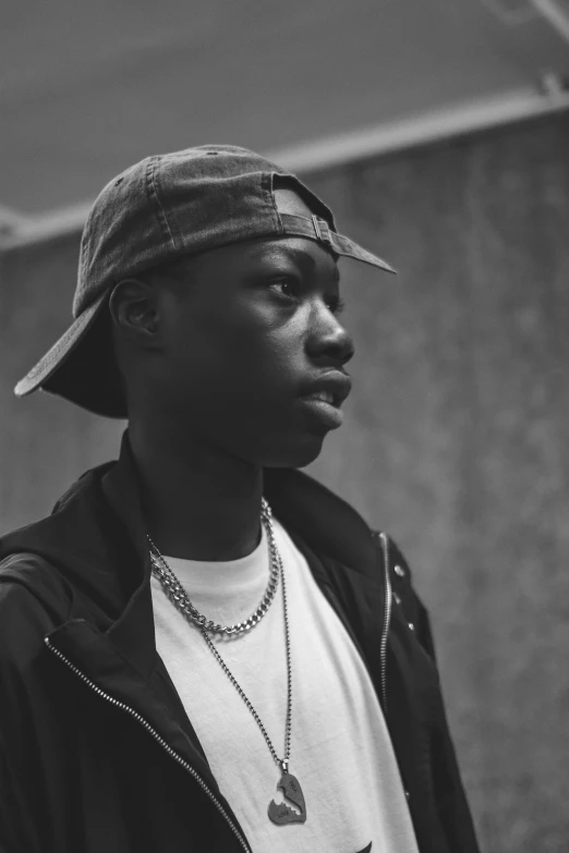 a black and white photo of a man wearing a hat, an album cover, by Bascove, trending on pexels, realism, black teenage boy, looking left, smol, anton