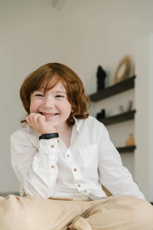 a little girl sitting on top of a bed, wearing a white button up shirt, red haired teen boy, portrait featured on unsplash, grinning lasciviously