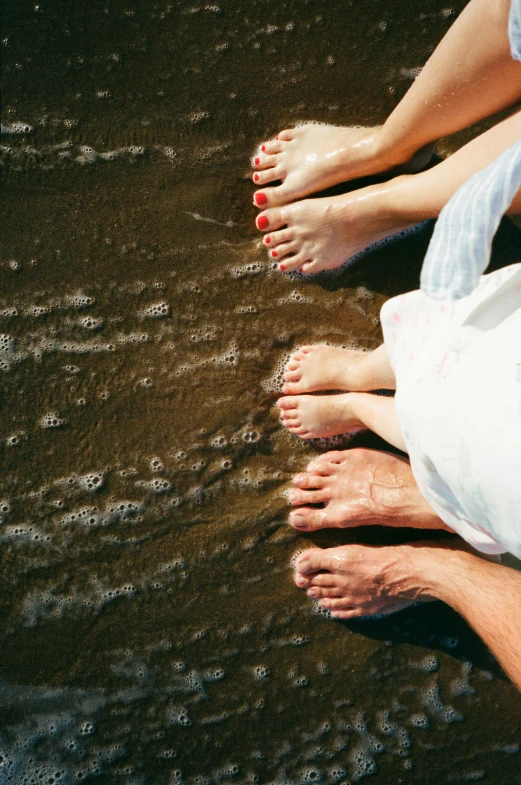 a couple of people that are standing in the water, exposed toes, from above, soft-sanded coastlines, real human feet